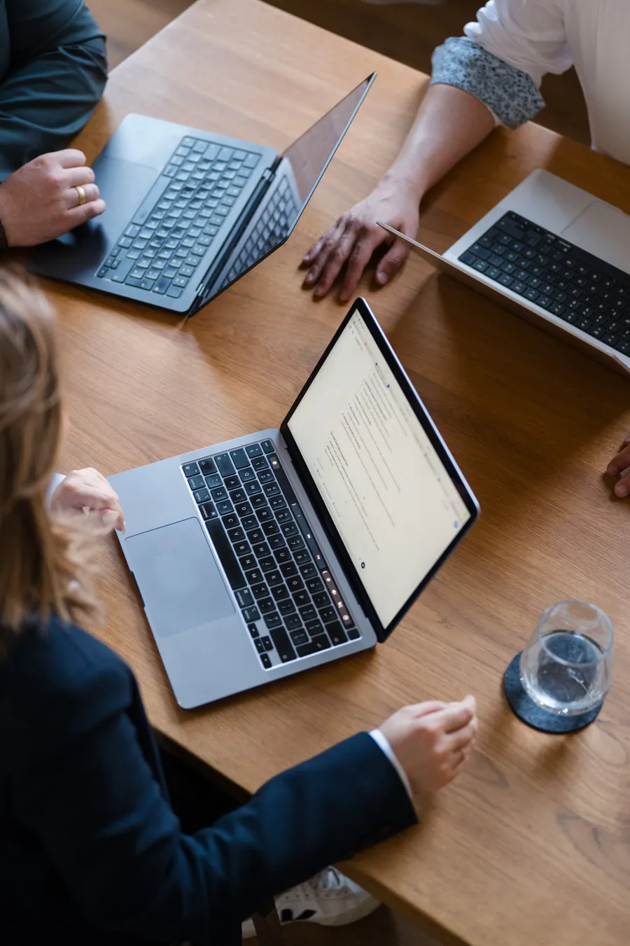 Laptops auf einem Holztisch von oben, drei Personen arbeiten zusammen
